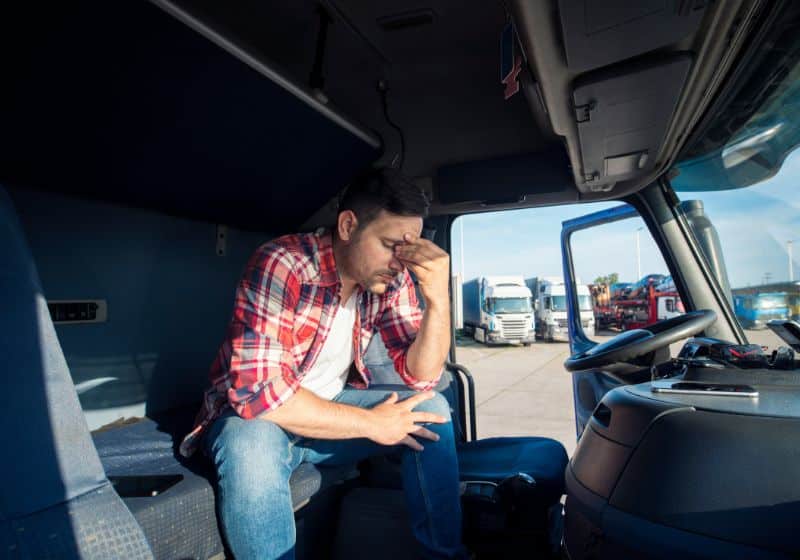 imagem de um homem sentado em um bando de um caminhão com a mão na cabeça 